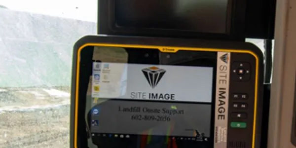Close-up of a rugged tablet displaying SITE IMAGE and contact info for landfill support, set against a blurred background of landfill